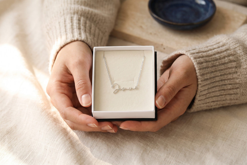 Hands holding an open gift box with a name necklace