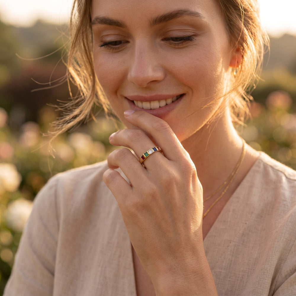 Smiling woman in golden light wearing a gold ring set with colorful birthstones