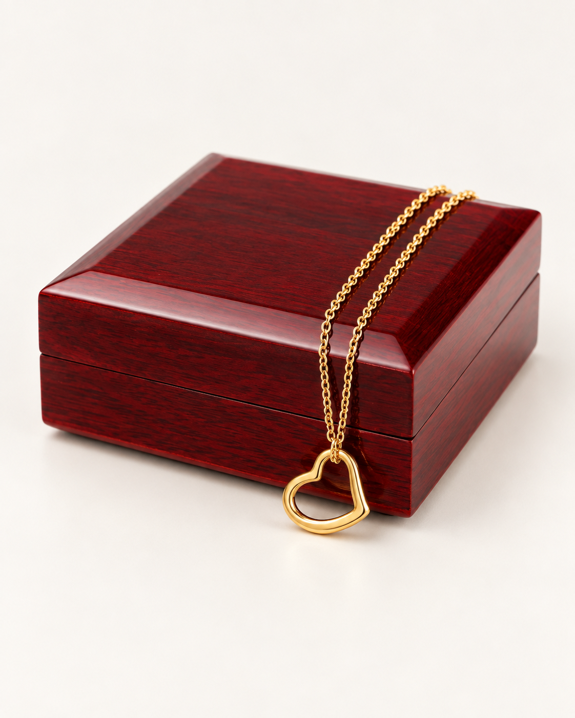 Delicate gold-finish heart necklace draped across a wooden gift box.