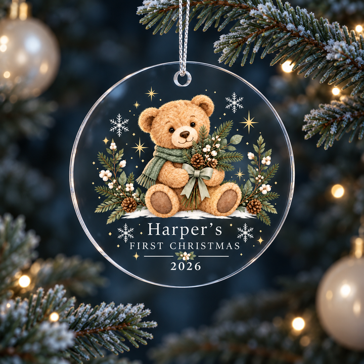Clear acrylic first Christmas ornament with an evergreen-scarf teddy and example name Harper, hanging on a tree.