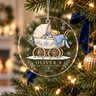 Clear acrylic first Christmas ornament with a teddy in a blue pram and example name Oliver, hanging on a lit tree.