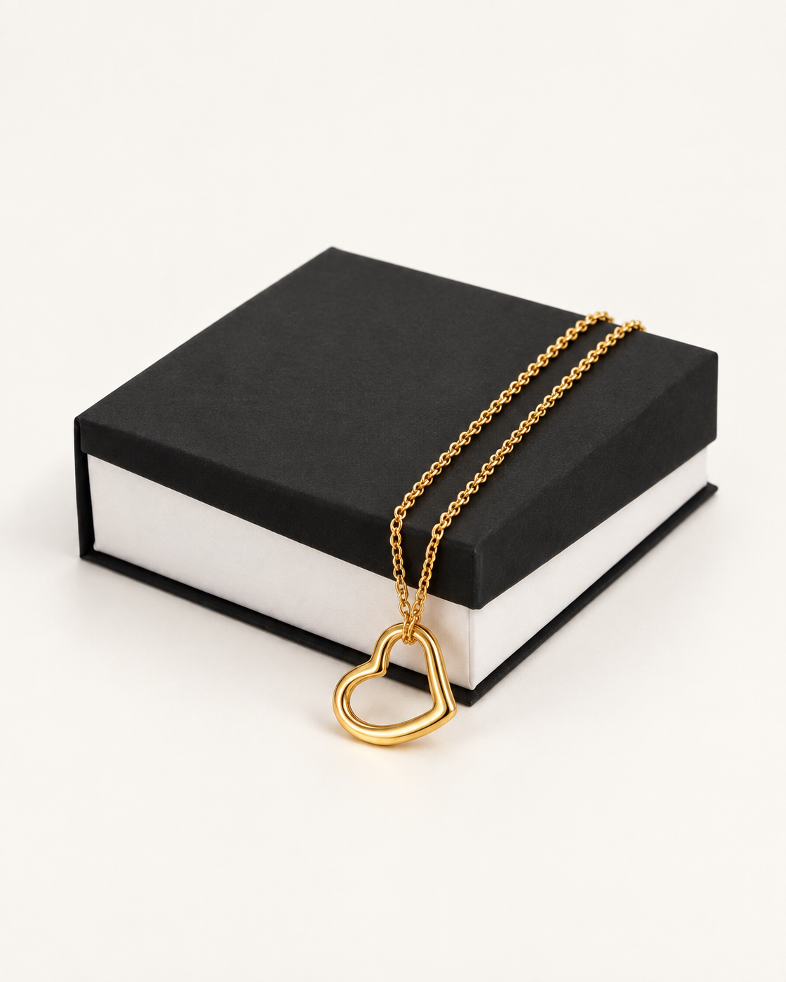 Delicate gold-finish heart necklace draped across a black gift box.