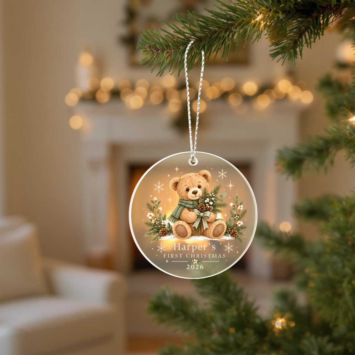 Evergreen teddy first Christmas ornament hanging from a tree in a softly lit living room.