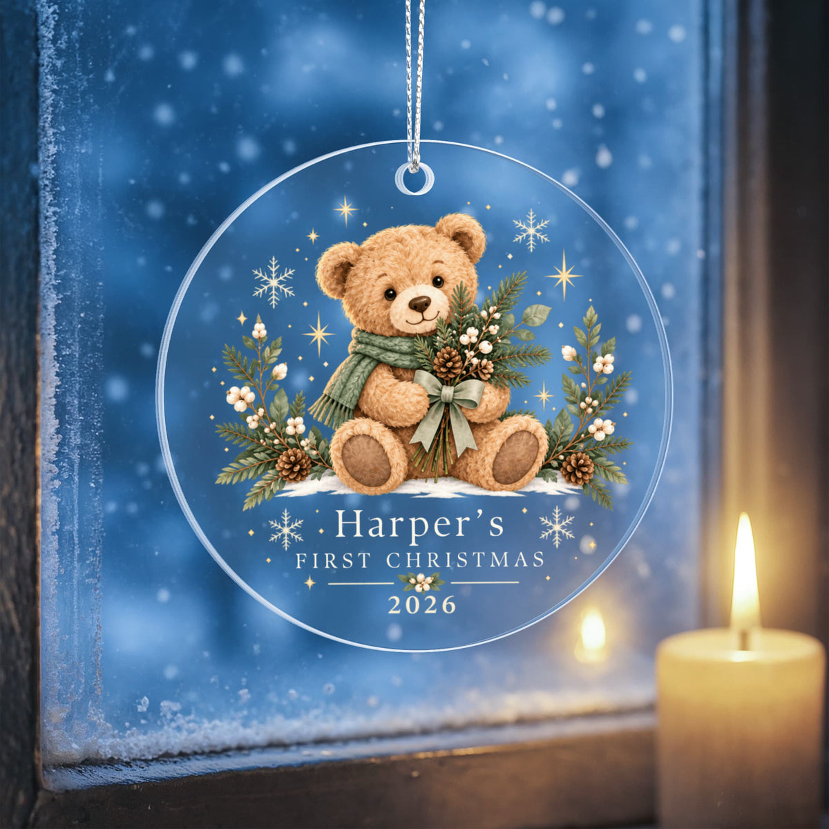 Evergreen teddy first Christmas ornament against a wintry blue background beside a candle.