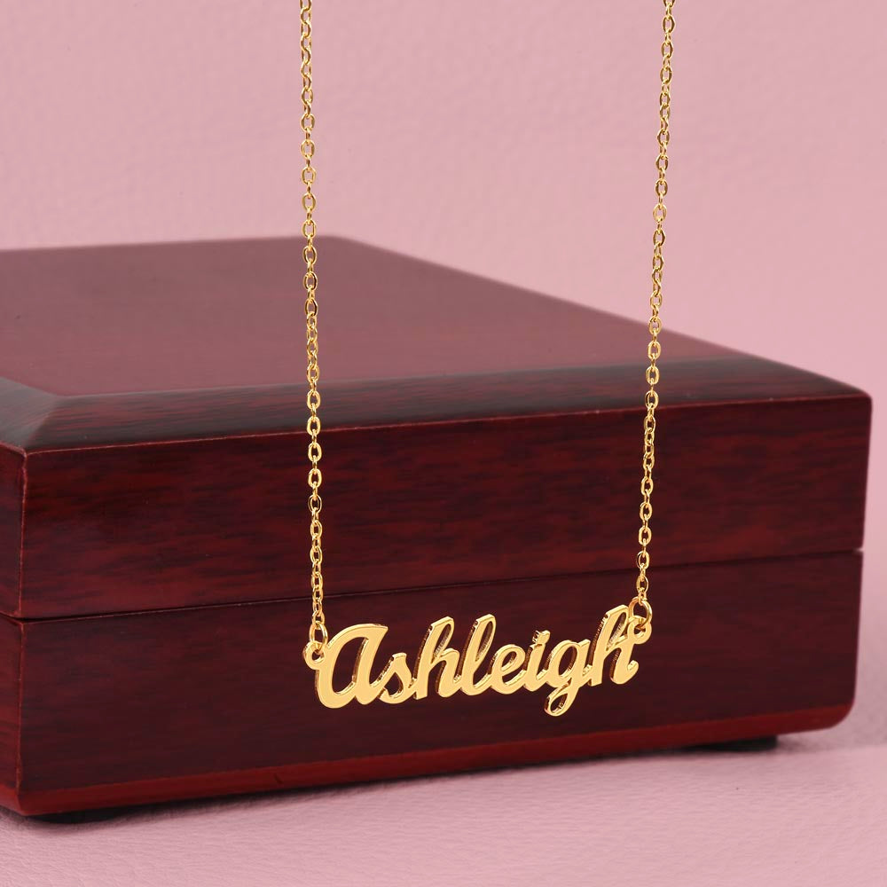 Gold-tone Ashleigh script name necklace displayed against a wooden gift box.