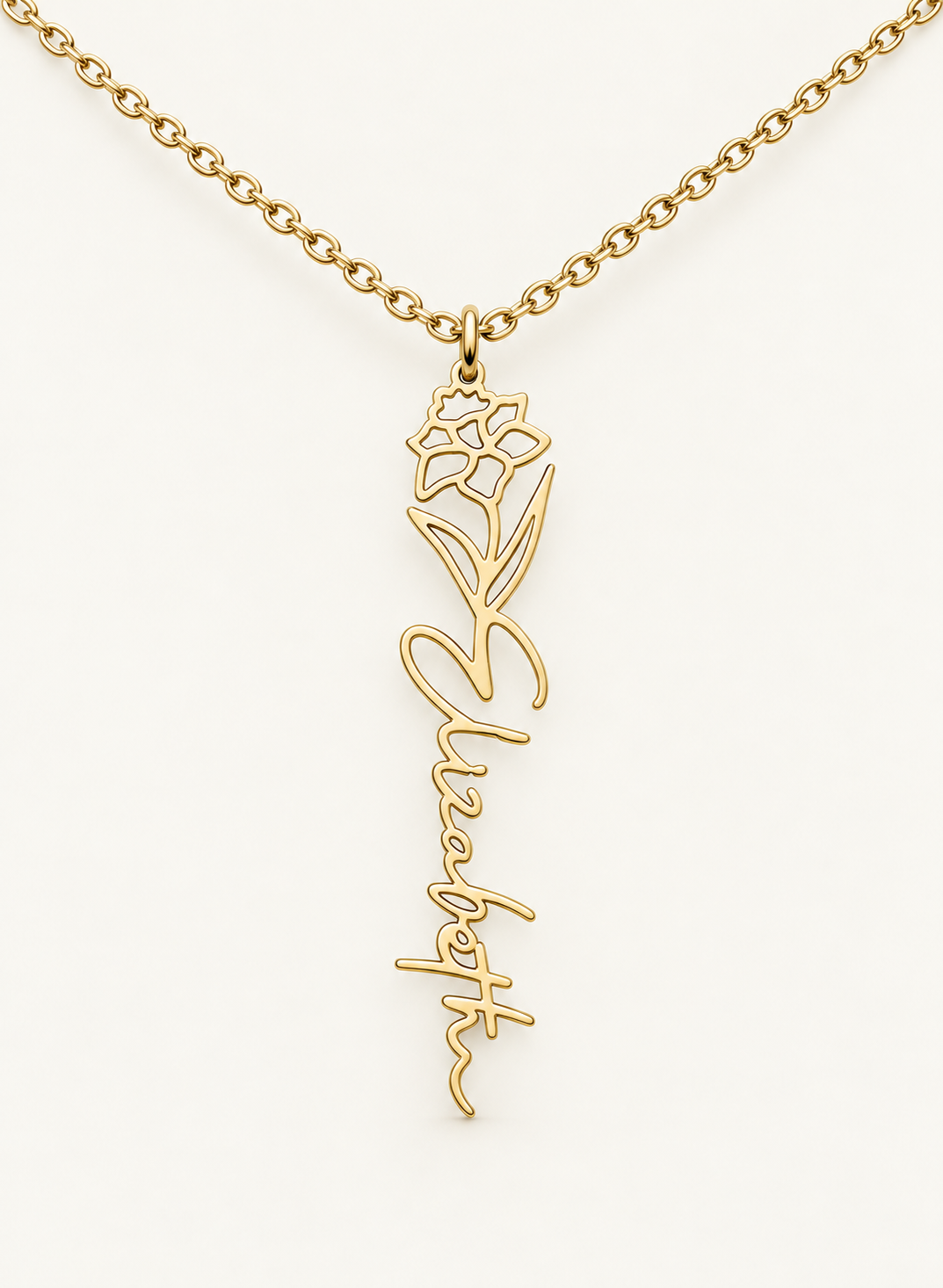 Gold-tone birth flower necklace with a narcissus motif and vertical script name pendant on ivory.