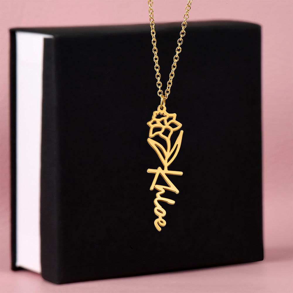 Gold-tone birth flower and vertical name necklace displayed on a black gift box.