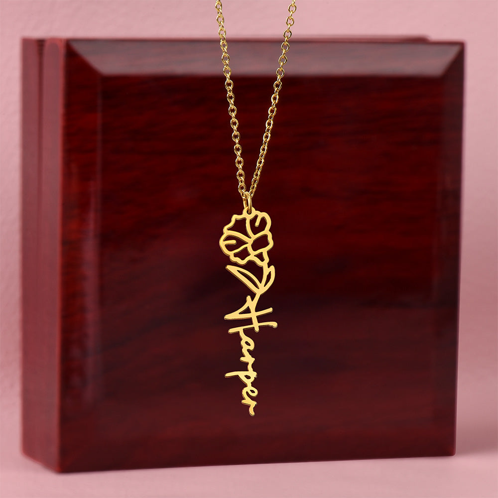 Gold-tone birth flower and vertical name necklace displayed on a wooden gift box.