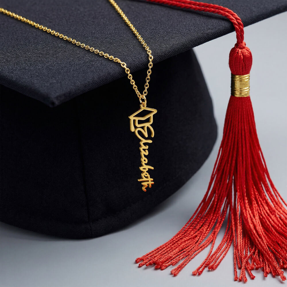 Gold-tone graduation name necklace draped on a black mortarboard with a red tassel.