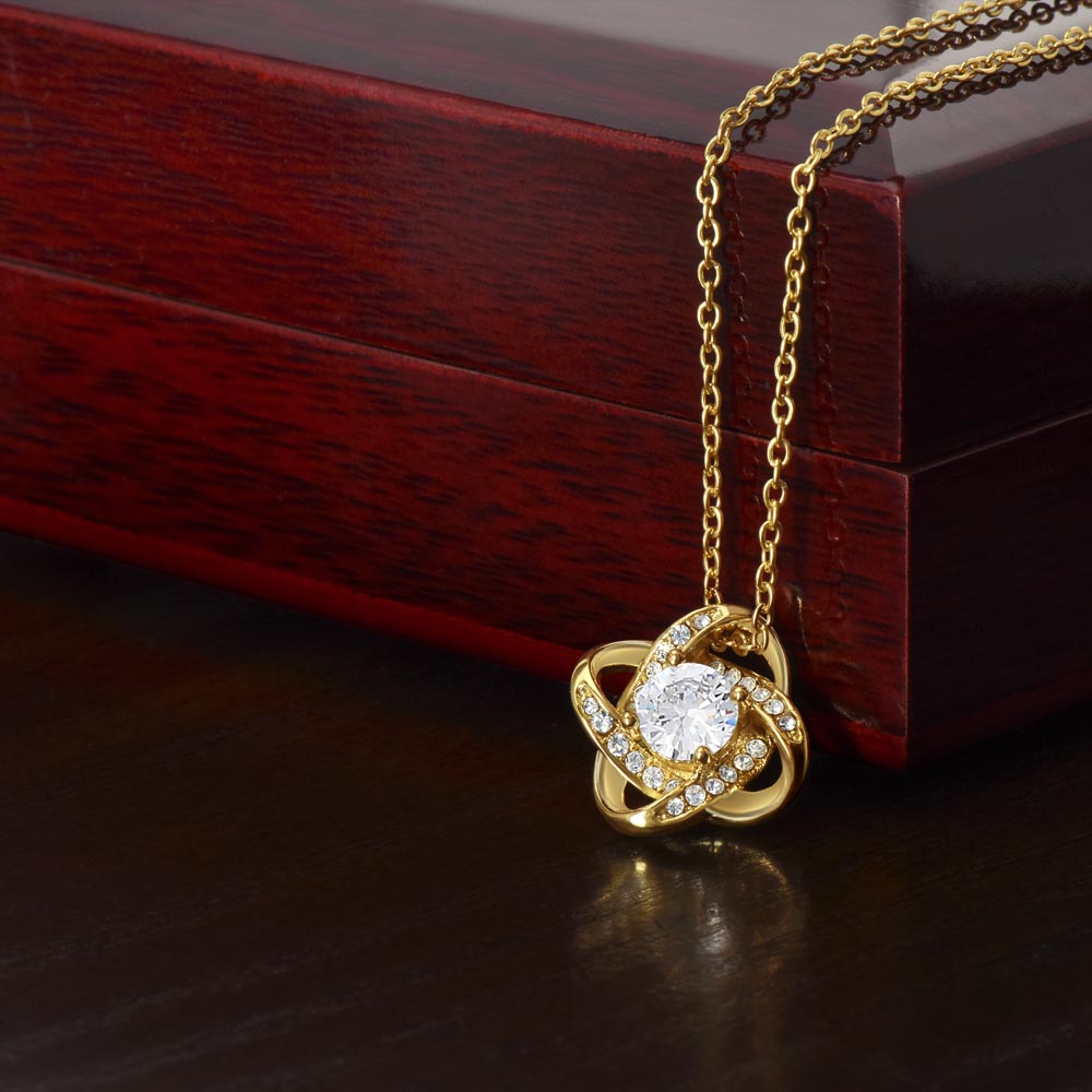 Gold-tone Love Knot CZ necklace displayed against a wooden gift box.