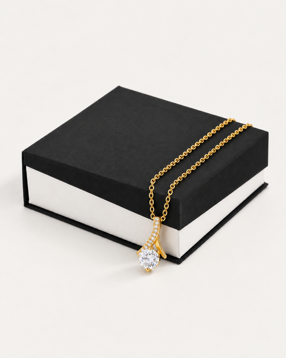 Gold-tone ribbon CZ necklace draped across a black gift box.