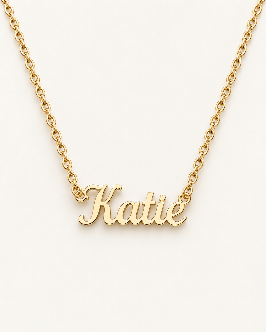 Gold-tone script name necklace with the example name Katie on ivory.