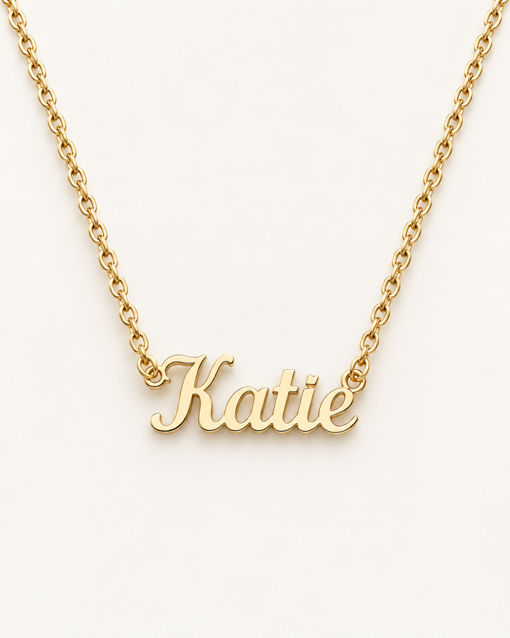 Gold-tone script name necklace with the example name Katie on ivory.