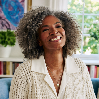 Woman smiling outdoors in an ivory knit cardigan.