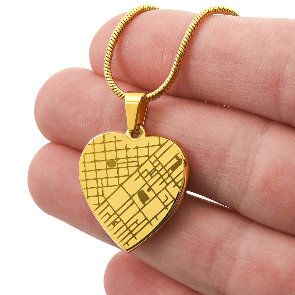 Hand holding a gold-tone engraved heart map pendant to show its scale.