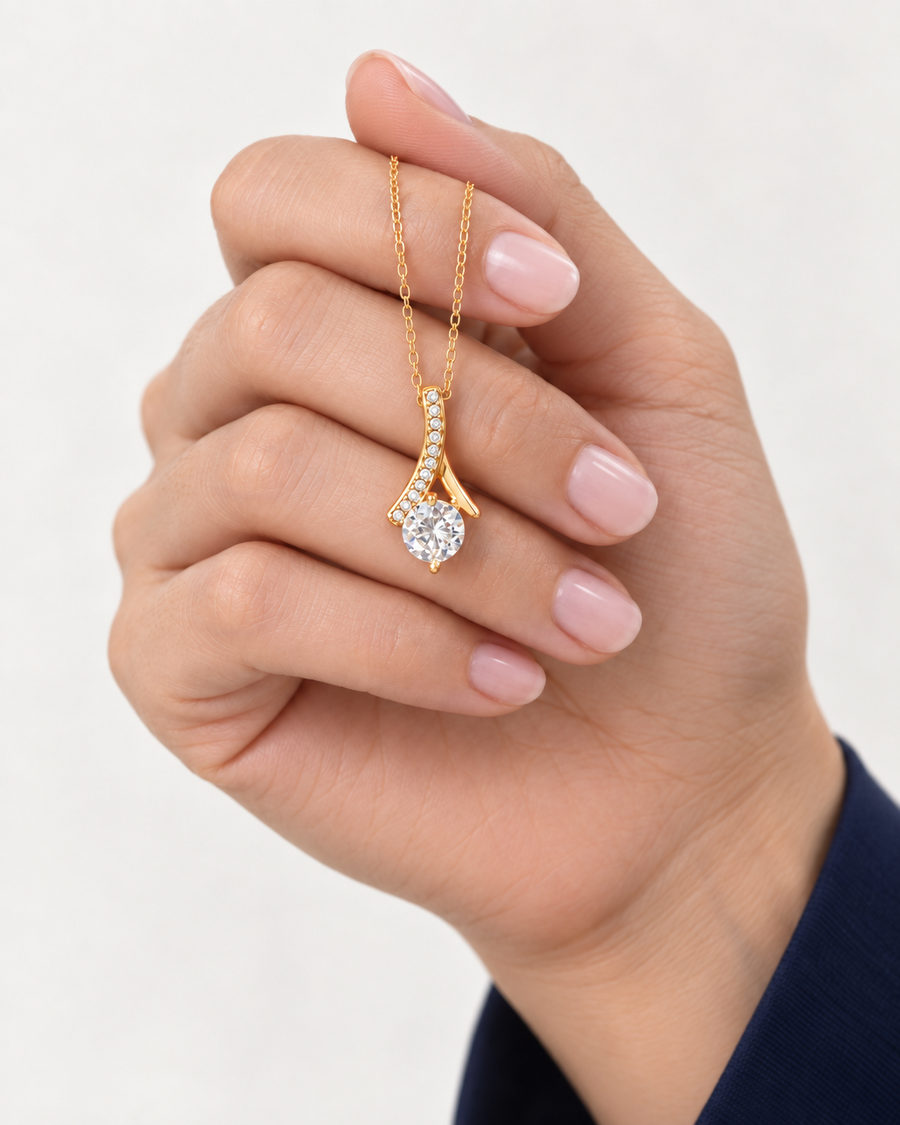 Hand holding a gold-tone ribbon CZ necklace to show the pendant's scale.