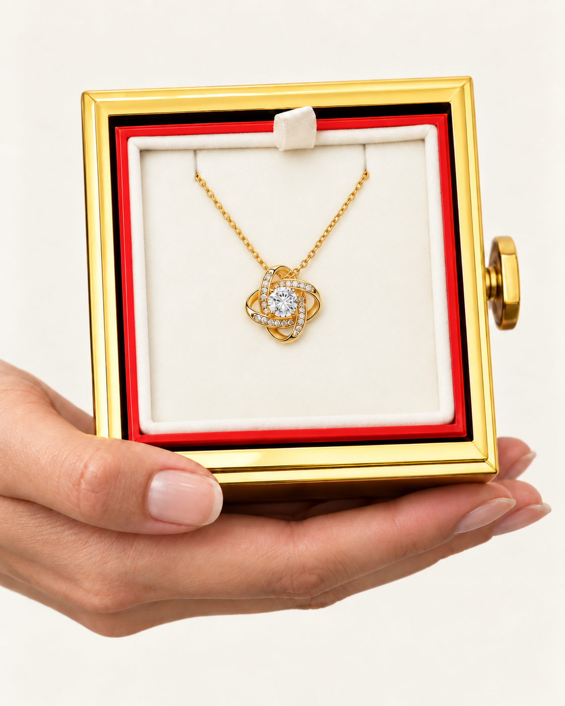 Hand holding an open rotating rose box with a gold-tone Love Knot necklace inside.