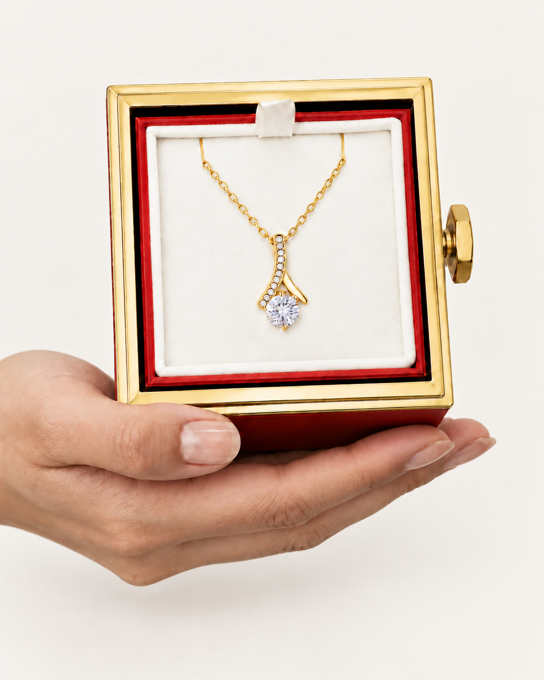 Hand holding an open rotating rose box with a gold-tone ribbon CZ necklace inside.