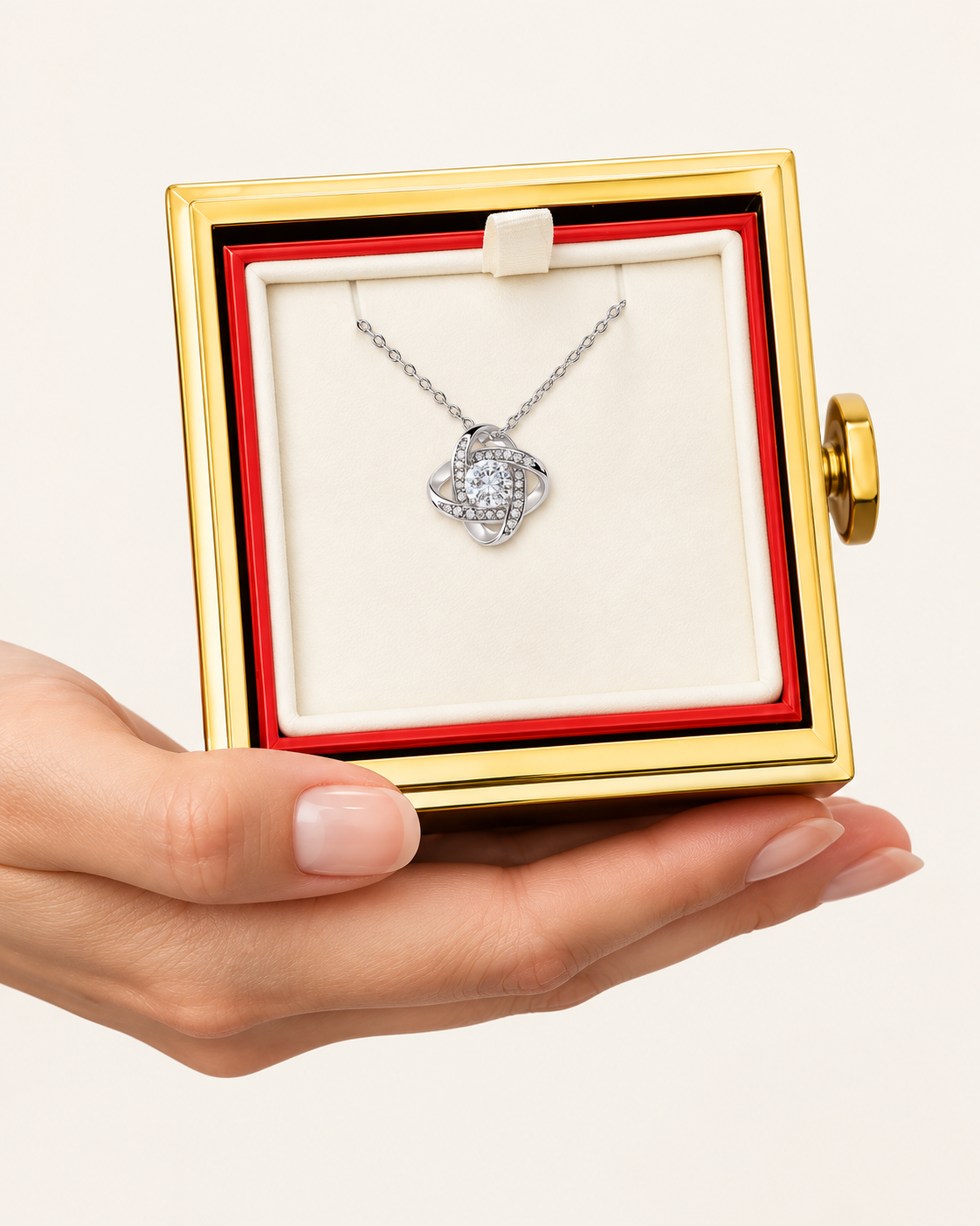 Hand holding an open rotating rose box with a silver-tone Love Knot necklace inside.