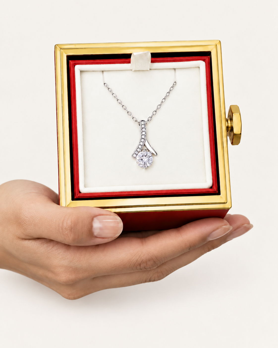 Hand holding an open rotating rose box with a silver-tone ribbon CZ necklace inside.