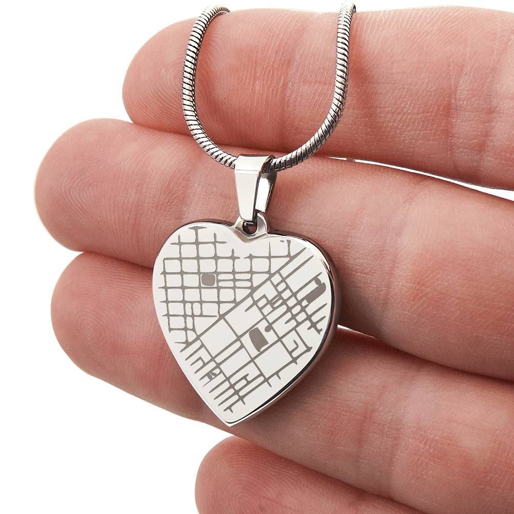Hand holding a silver-tone engraved heart map pendant to show its scale.