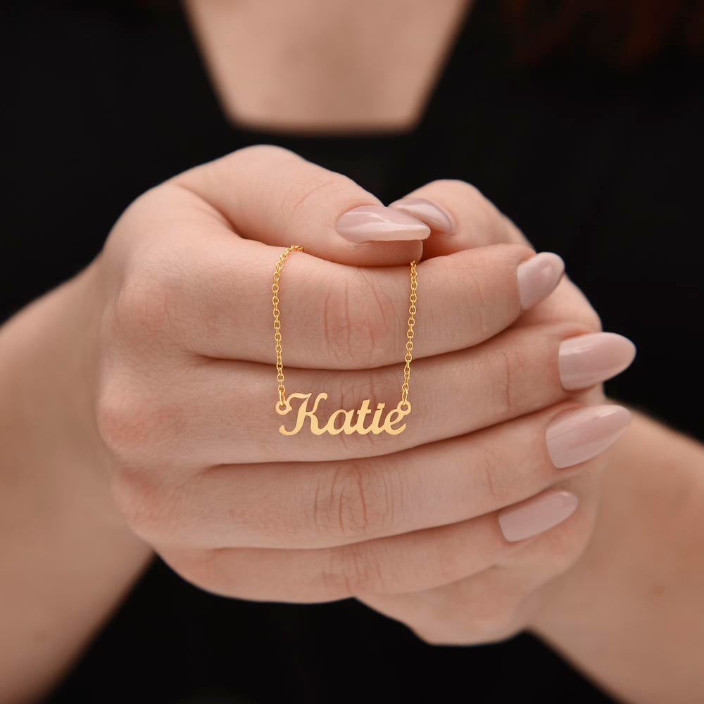 Hands holding a gold-tone Katie script name necklace.