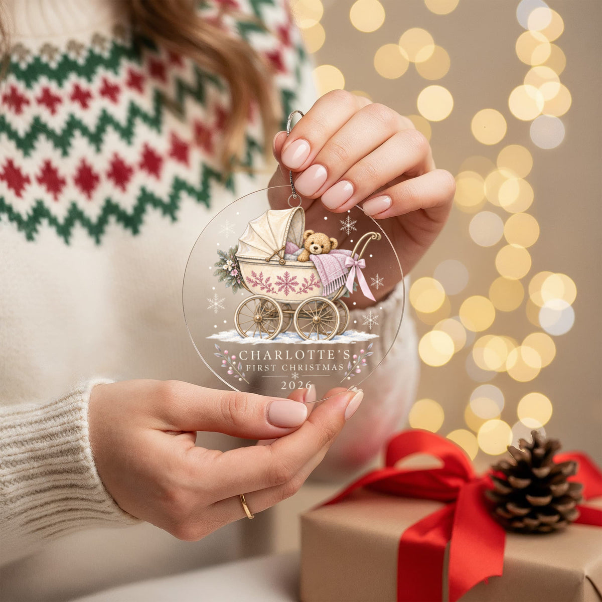 Hands holding a pink teddy pram first Christmas ornament with the example name Charlotte.