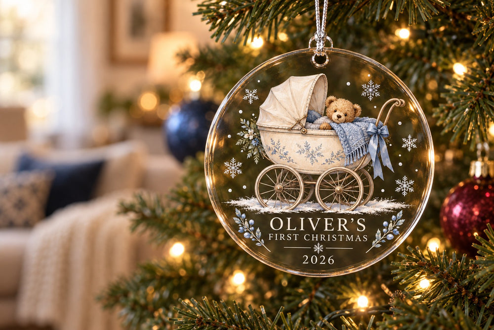 Personalized blue teddy pram first Christmas ornament hanging on a warmly lit tree.