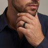 Man wearing a black engraved band with his hand resting near his chin.