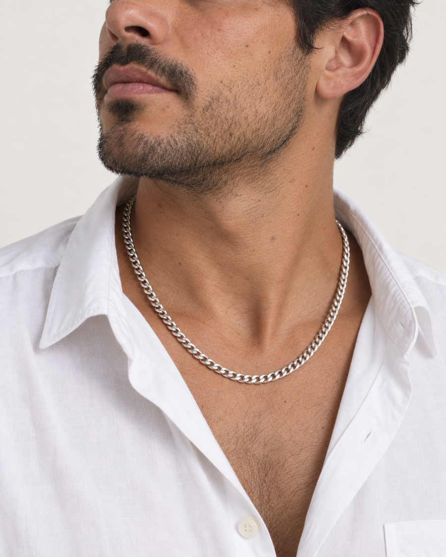 Man wearing a silver-tone Cuban link necklace with a white shirt.