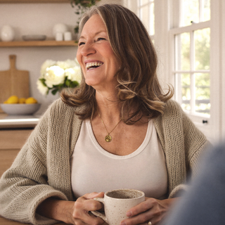 Woman laughing with a mug in her hands in a bright living room.