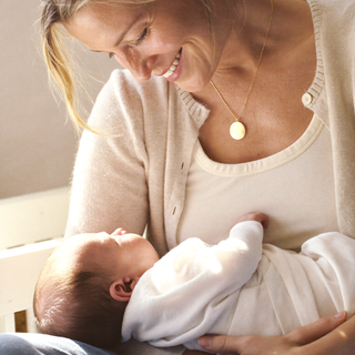 Woman wearing a pendant necklace while holding a sleeping baby.