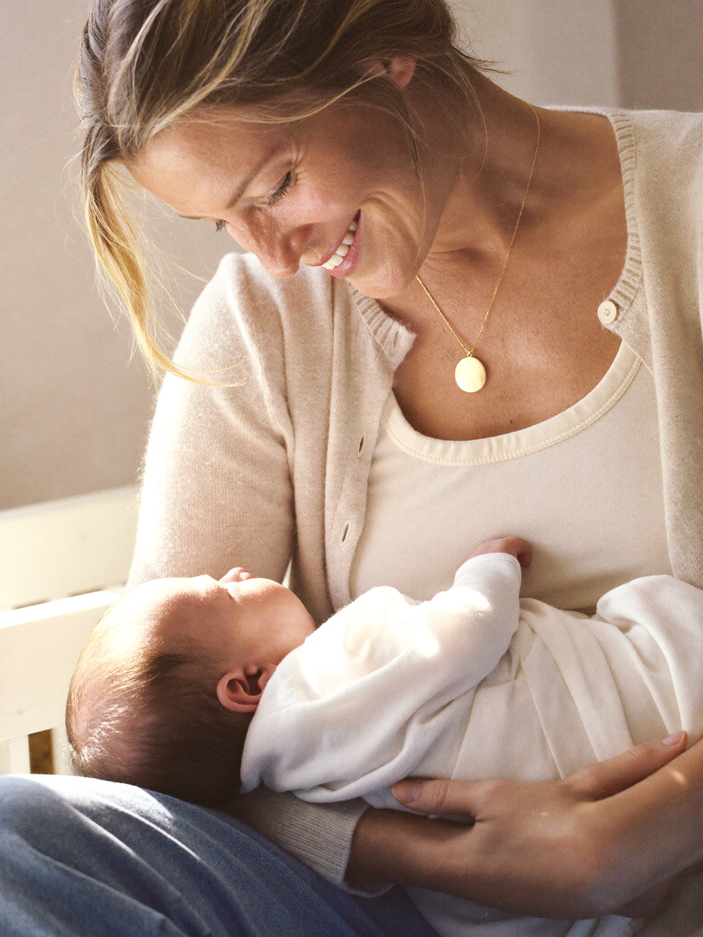 Woman wearing a pendant necklace while holding a sleeping baby.