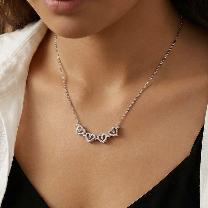 Close-up of the open four-heart necklace worn with a black top and white shirt.