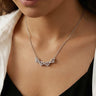 Close-up of the open four-heart necklace worn with a black top and white shirt.