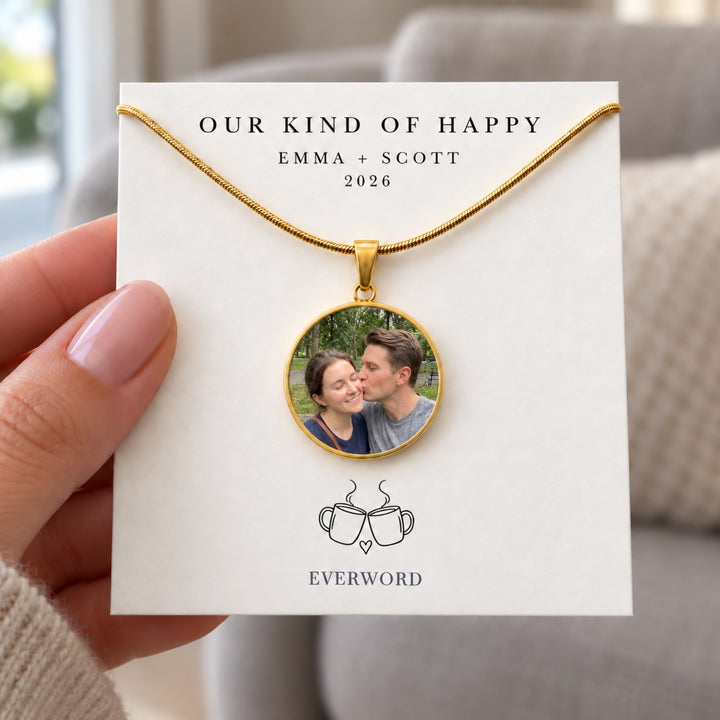 Hand holding an Everword gold-tone photo necklace on an Emma + Scott personalized coffee-themed story card.