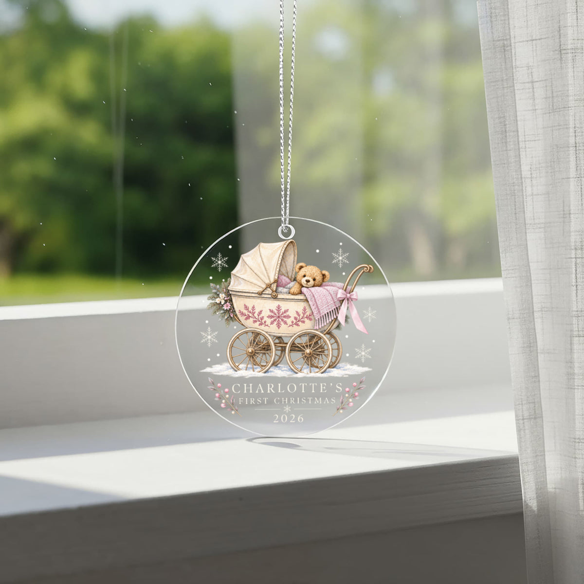Pink teddy pram first Christmas ornament hanging in front of a bright window.