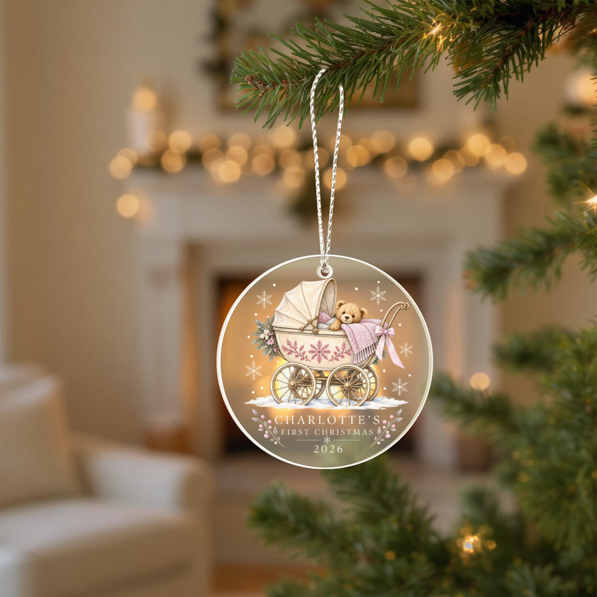 Pink teddy pram first Christmas ornament hanging from a tree in a softly lit living room.