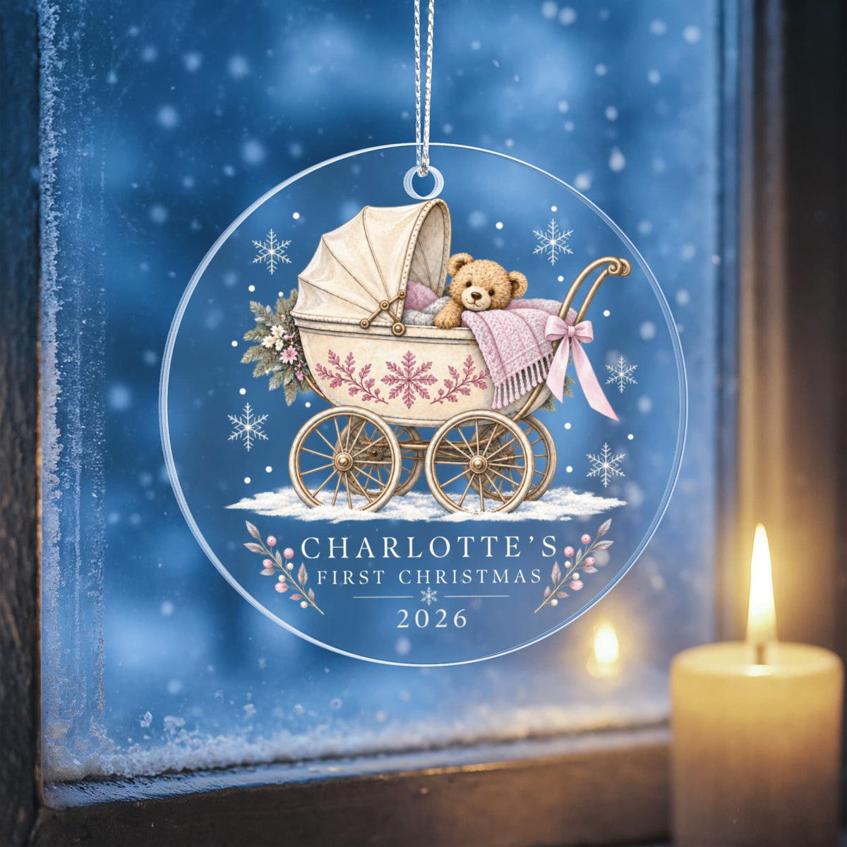 Pink teddy pram first Christmas ornament hanging against a wintry blue background beside a candle.