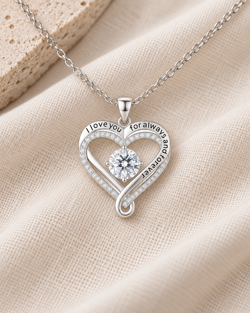 Silver-tone Love You Always heart CZ necklace resting on ivory fabric.