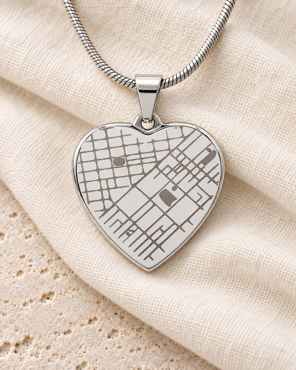 Silver-tone engraved heart map necklace resting on ivory fabric.