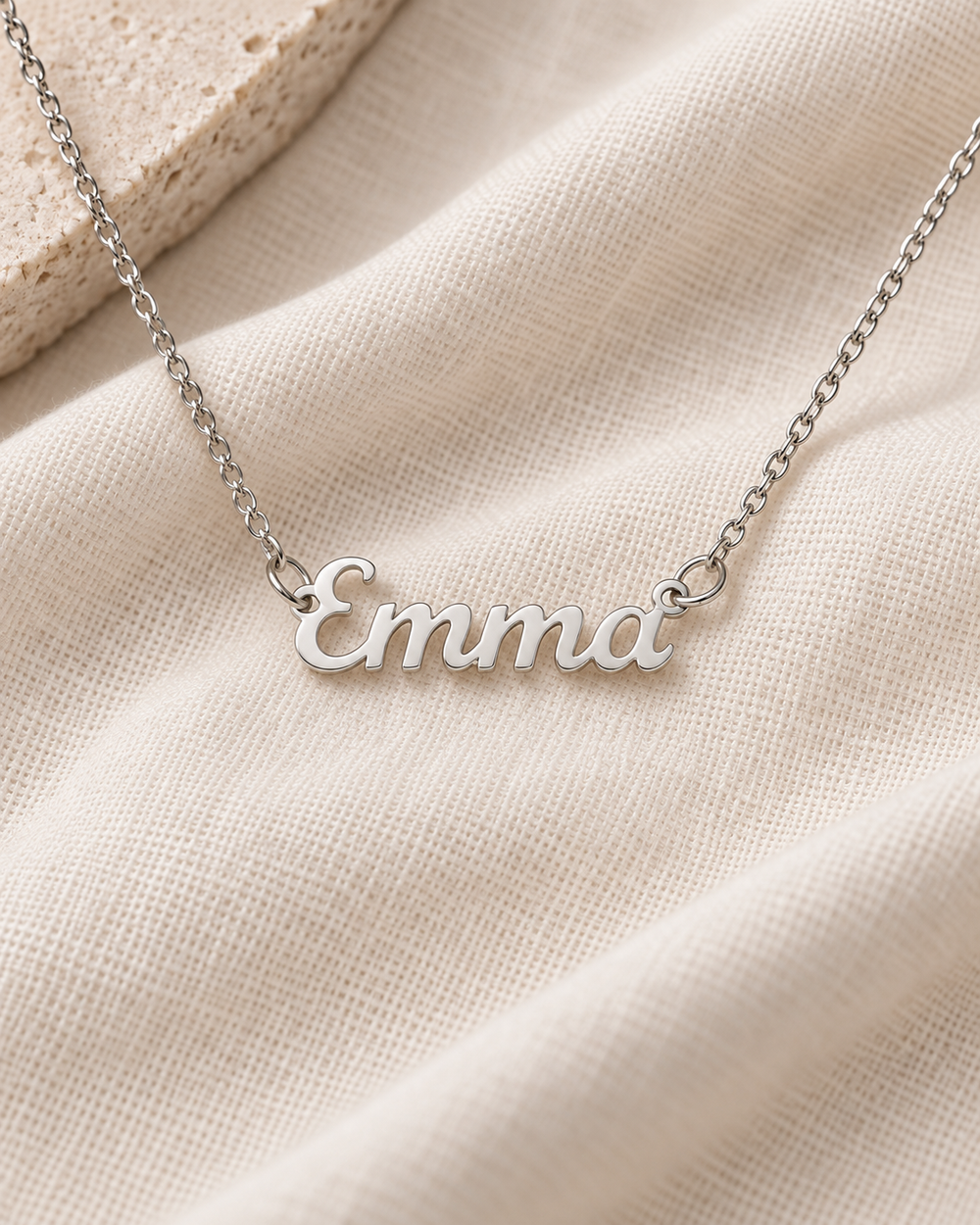 Silver-tone Emma script name necklace on ivory fabric.