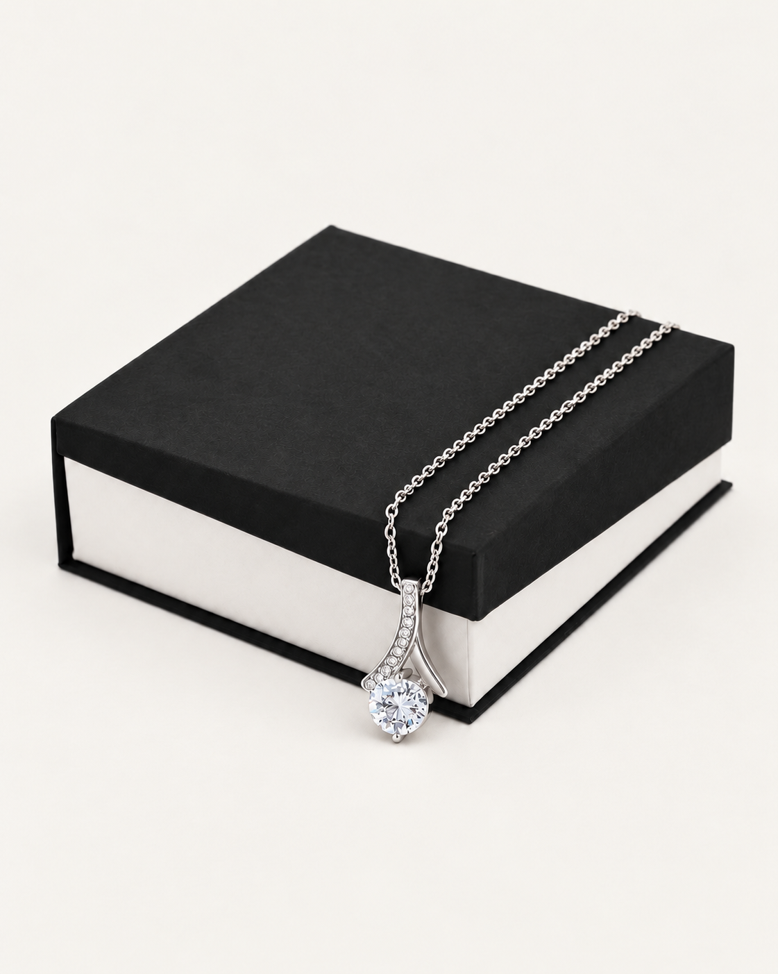 Silver-tone ribbon CZ necklace draped across a black gift box.