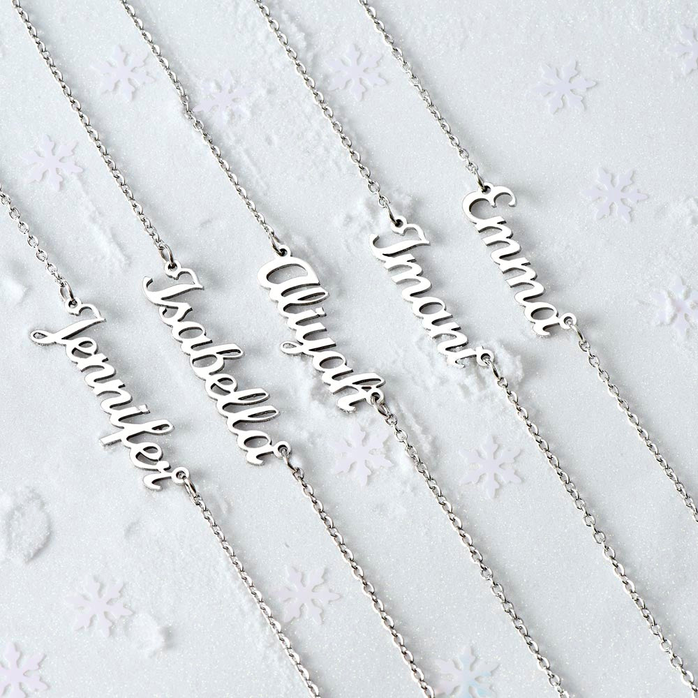 Several silver-tone script name necklaces arranged on pale fabric.