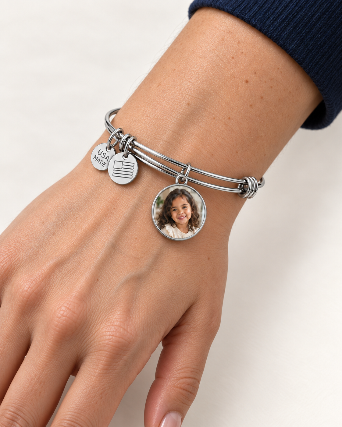 Silver-tone bangle with a round photo charm worn on a wrist.