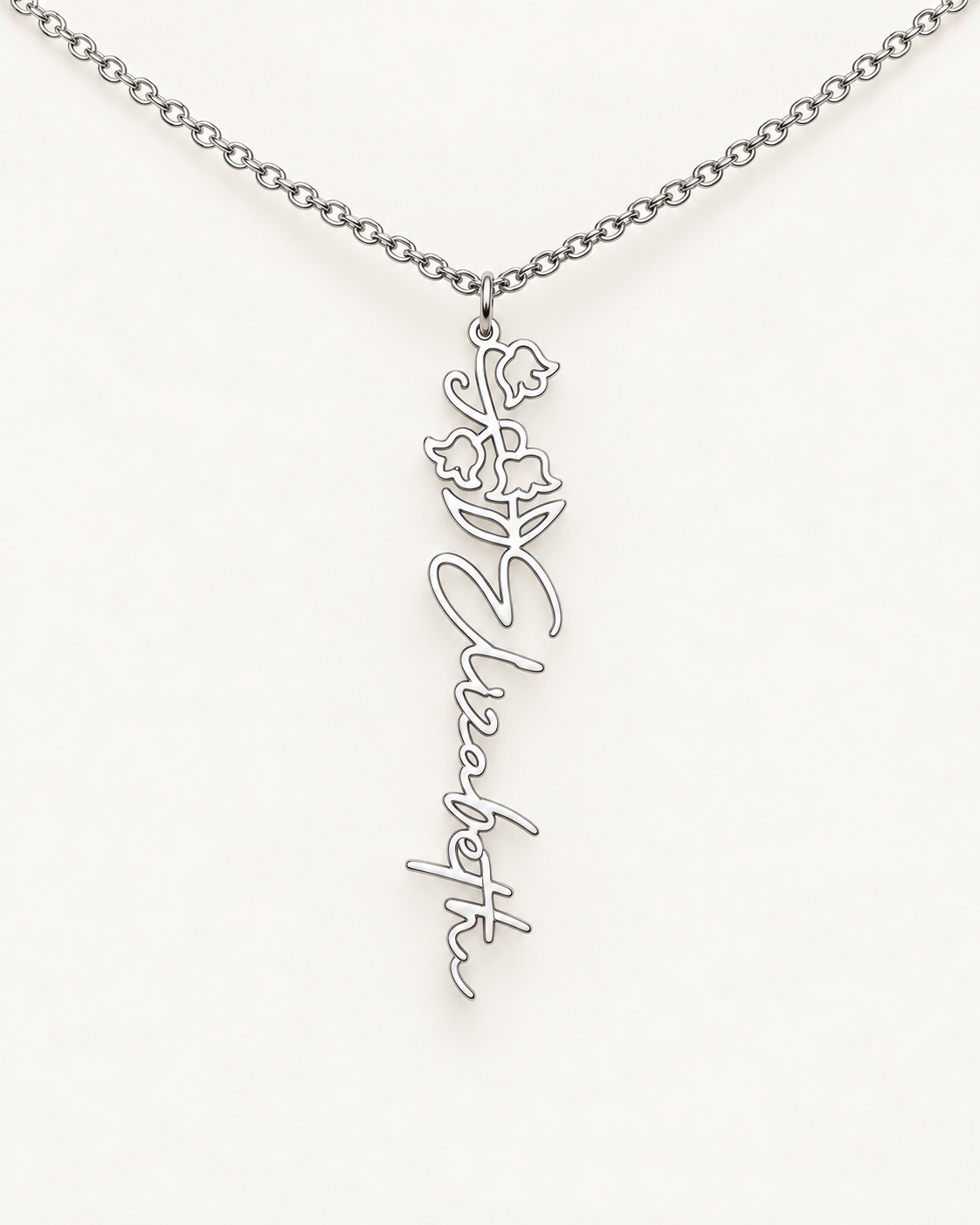 Silver-tone birth flower necklace with a lily of the valley motif and vertical script name pendant on ivory.