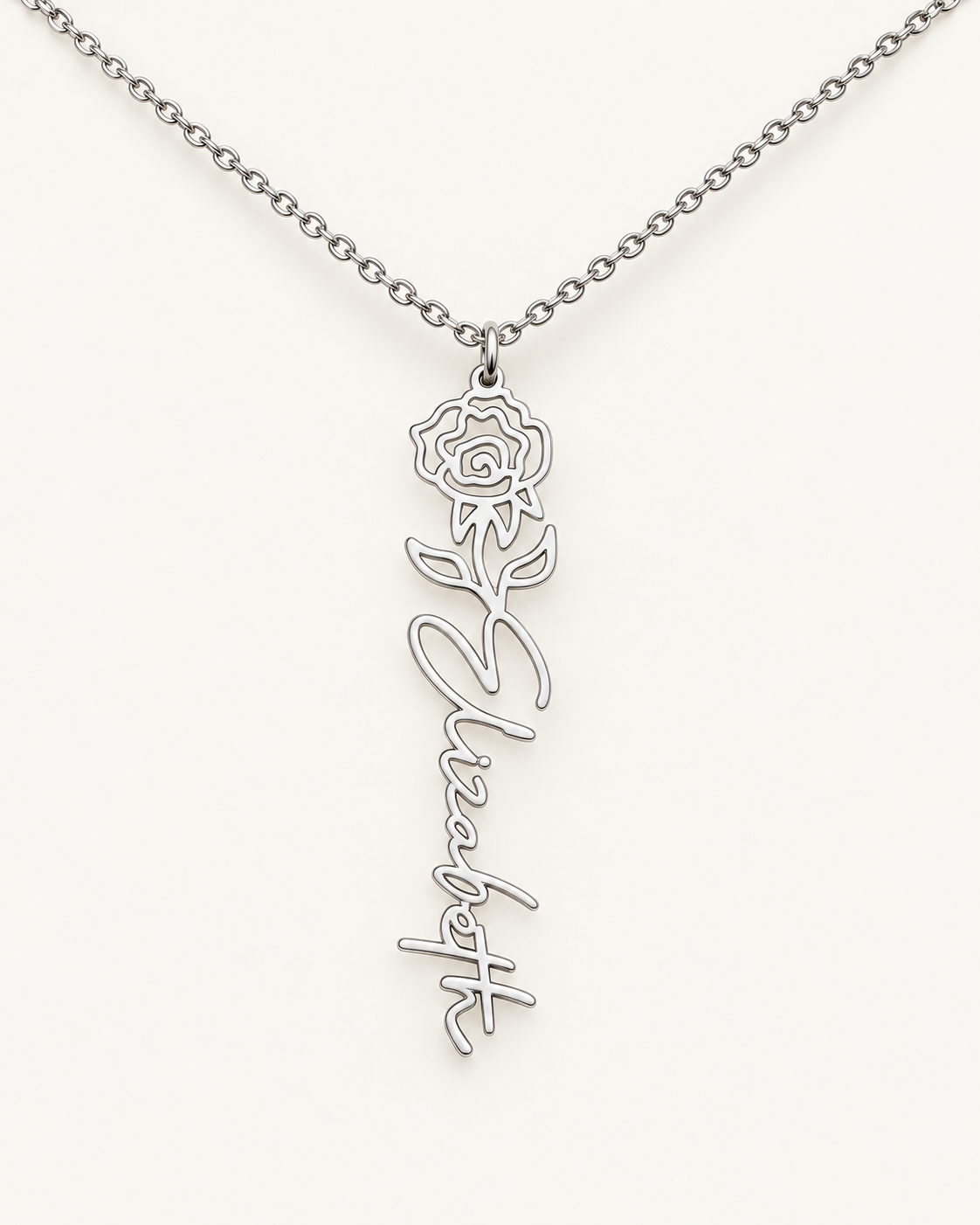 Silver-tone birth flower necklace with a rose motif and vertical script name pendant on ivory.