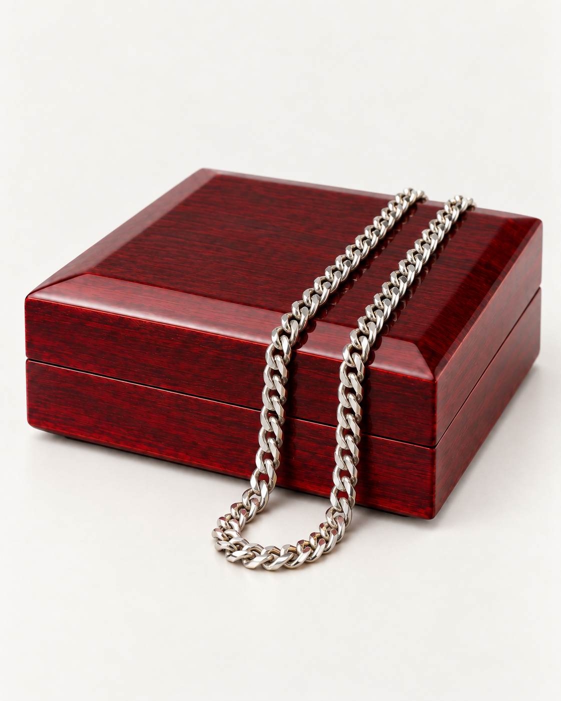 Silver-tone Cuban link chain draped across a wooden gift box.