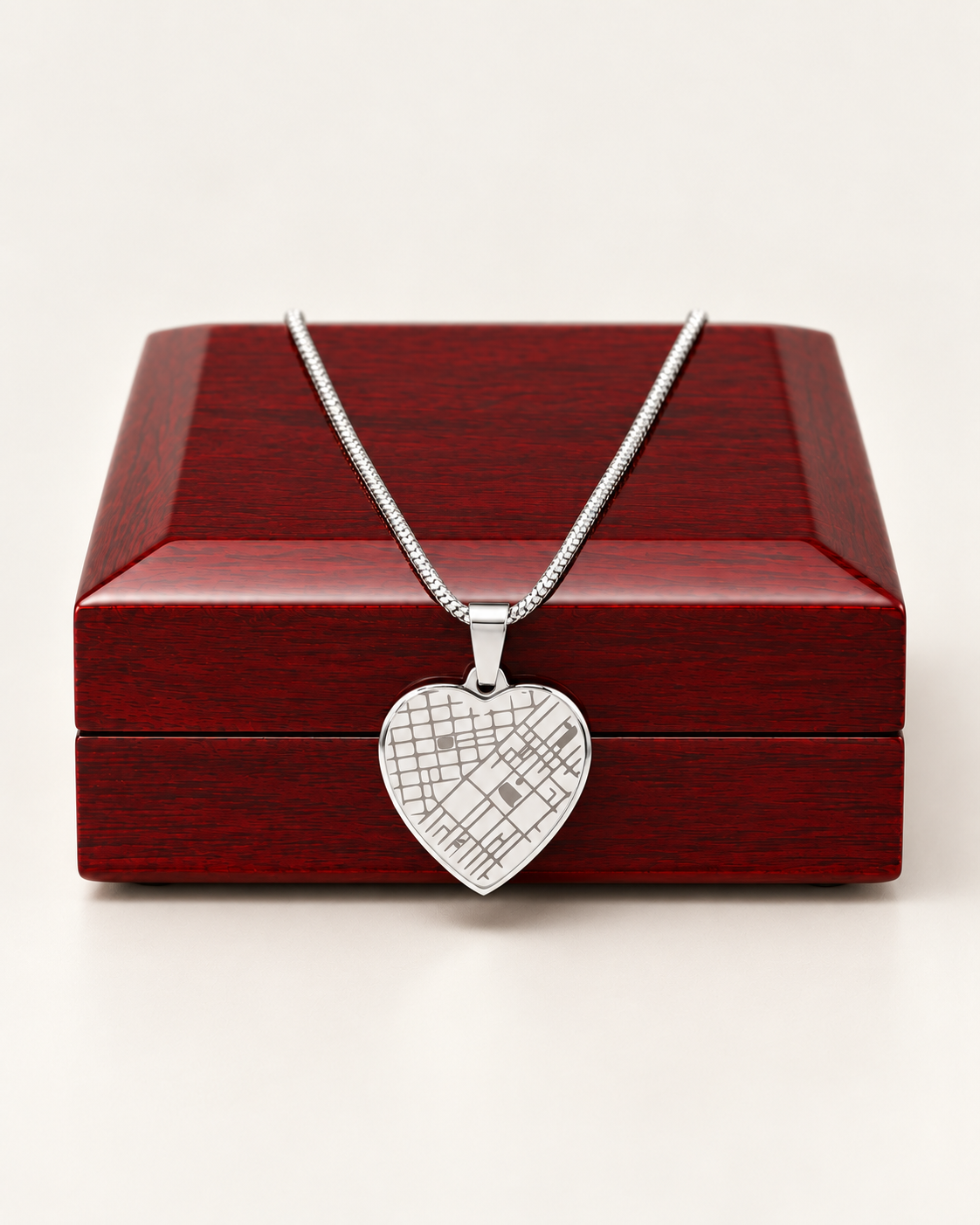Silver-tone heart map necklace draped across a wooden gift box.