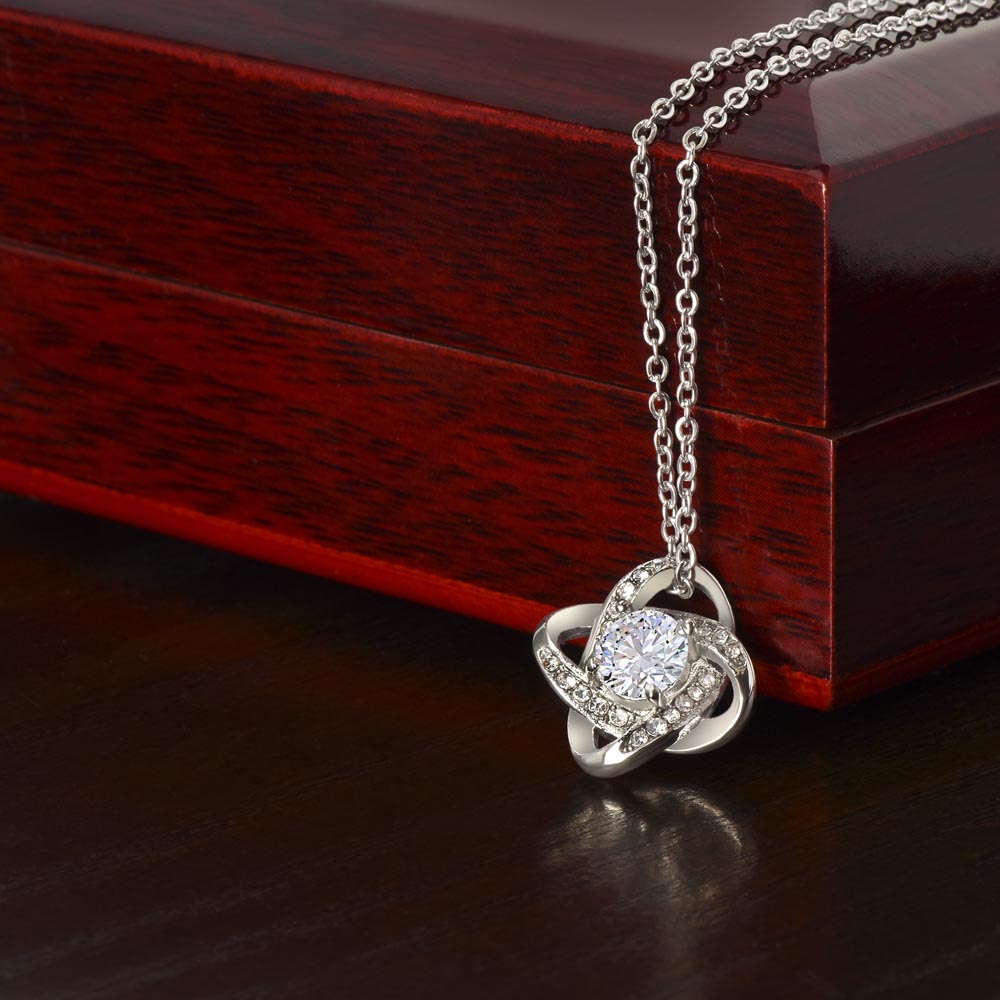 Silver-tone Love Knot CZ necklace displayed against a wooden gift box.